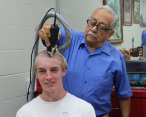 A young man receives a hair cut at MMA's military summer camp.